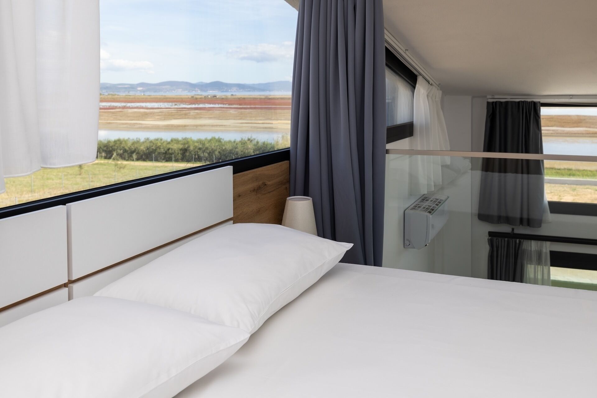 A bedroom with a bed, a window with curtains, and a view of a landscape.