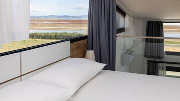 A bedroom with a bed, a window with curtains, and a view of a landscape.