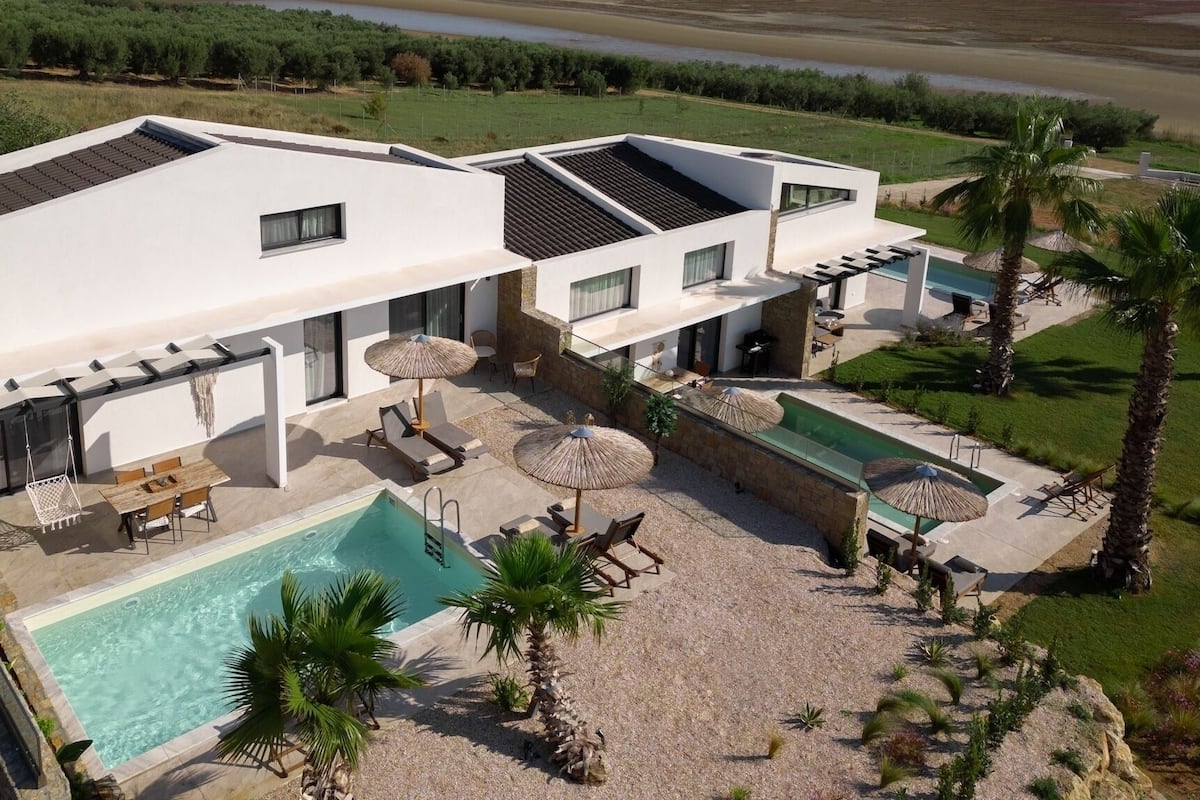 Una casa moderna de dos pisos amb piscina, mobiliari exterior i vistes a un riu.