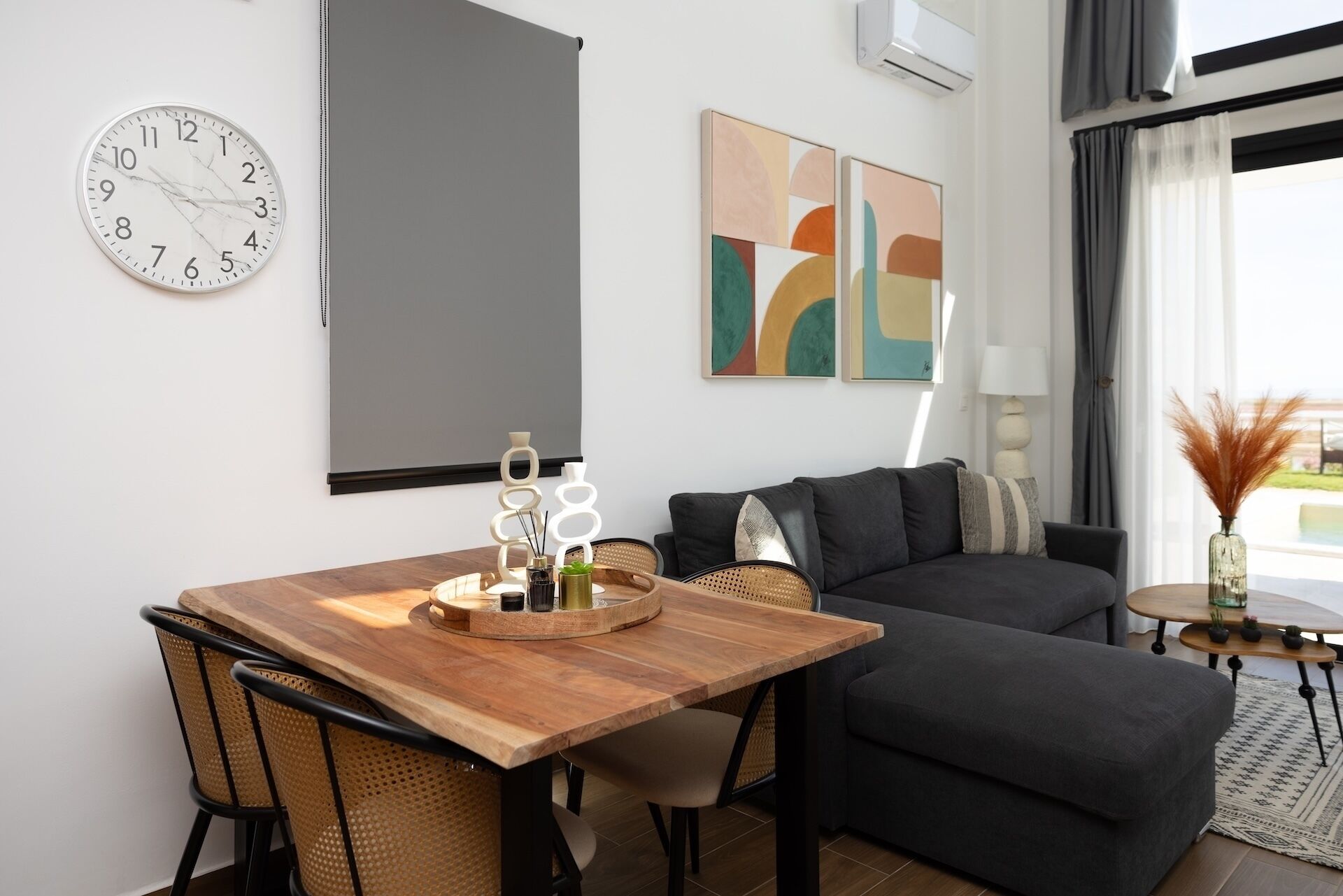 Una sala moderna con una mesa de comedor de madera, sofás negros y arte abstracto en la pared.