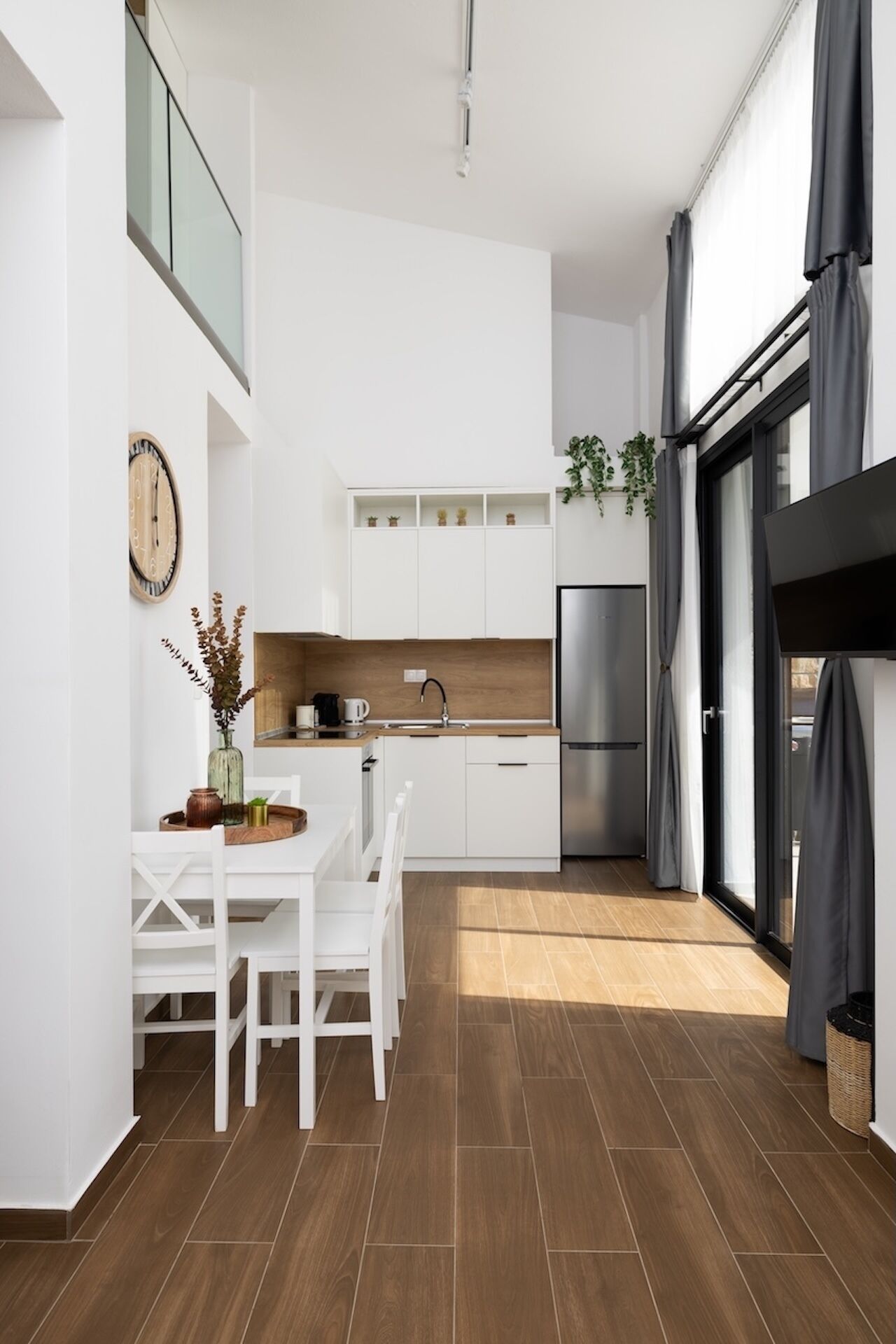 Eine moderne Küche mit weißen Schränken, einem Edelstahlkühlschrank und einem Essbereich mit weißem Tisch und Stühlen.