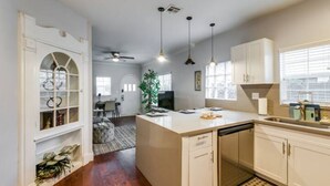 A modern kitchen with white cabinetry, a central island, pendant lights, and a dining area in the background.