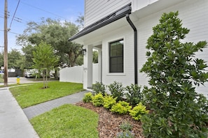 A residential house with a white exterior, a front porch, and a well-maintained lawn with shrubs and a small tree. - Lavish & Spacious Home in Walkable Hyde Park (Tampa)