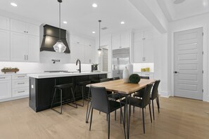 A modern kitchen with a central island, black bar stools, and white cabinetry. - Lavish & Spacious Home in Walkable Hyde Park (Tampa)