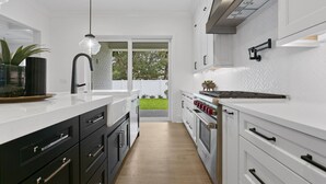 Une cuisine moderne avec des plans de travail blancs, des meubles de rangement noirs et blancs, des appareils électroménagers en acier inoxydable et une vue sur l’extérieur.