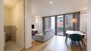 Ein modernes Wohnzimmer mit Sofa, Esstisch und Stühlen. Ein Fernseher und eine Lampe stehen auf einem Beistelltisch.