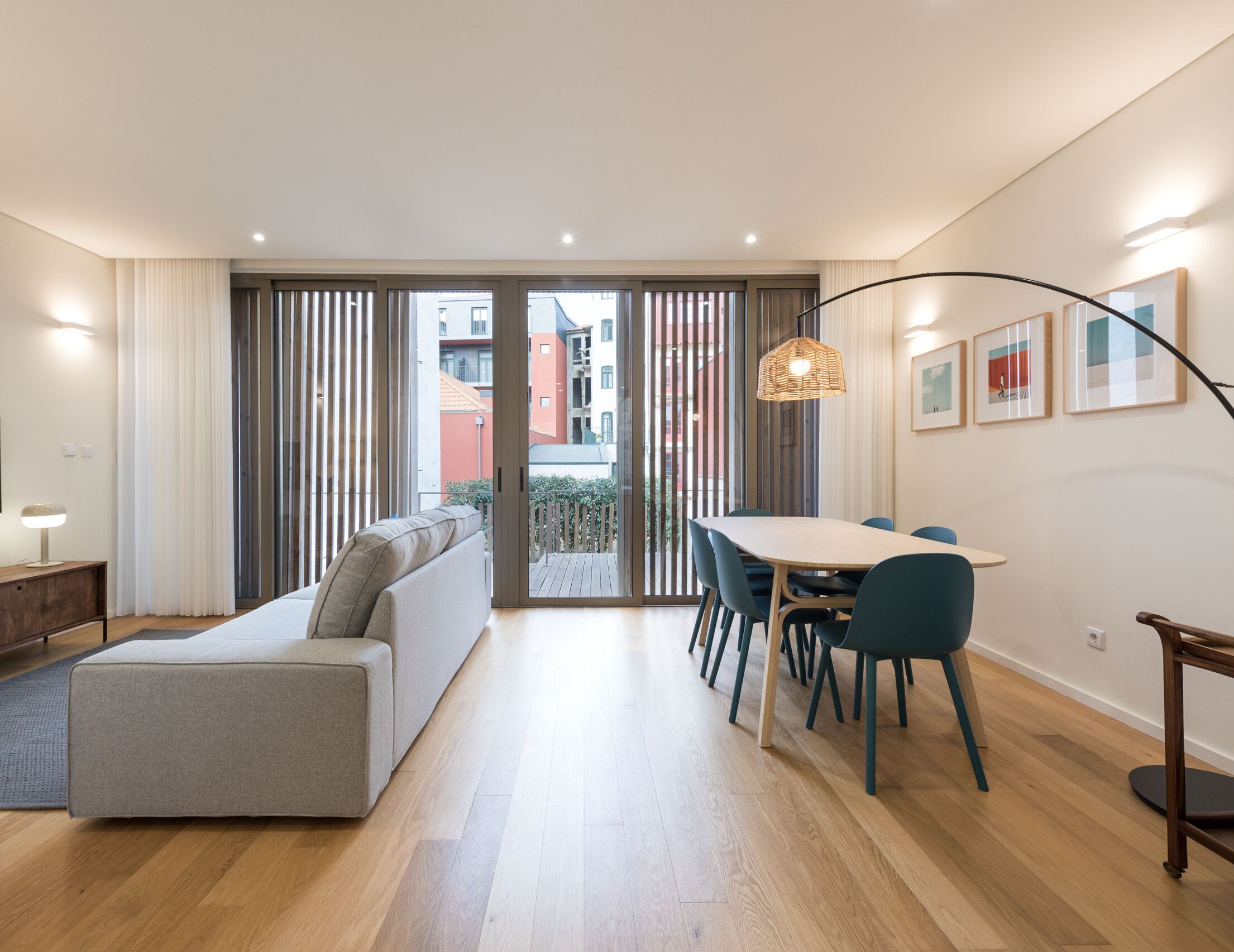A modern living room with a sofa, dining table, chairs, and a view through large sliding doors.