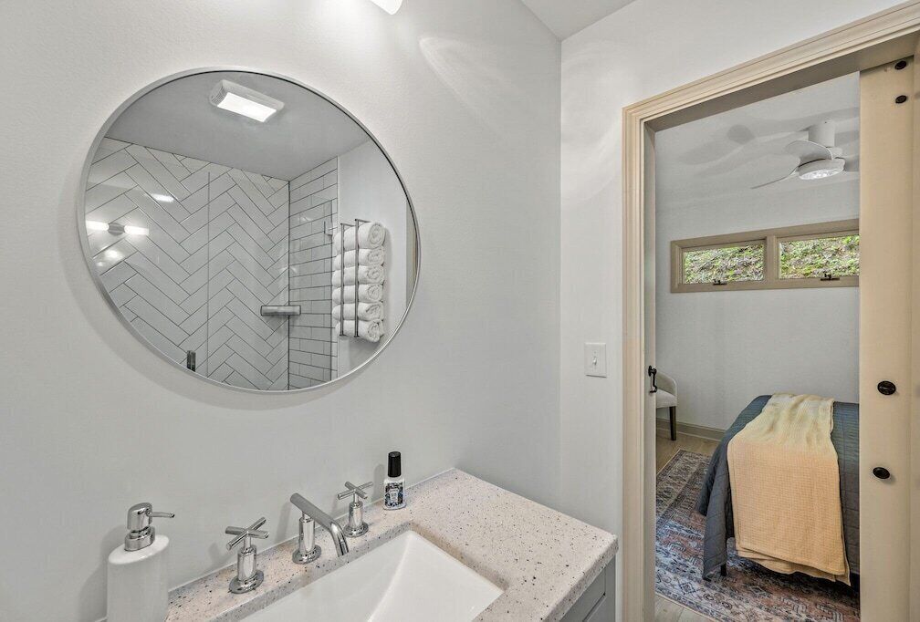 Un baño con un espejo redondo, un lavamanos con dos grifos y una zona de ducha con patrón de espiga.