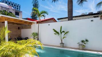 A swimming pool with a white wall, potted plants, and a wooden pergola.