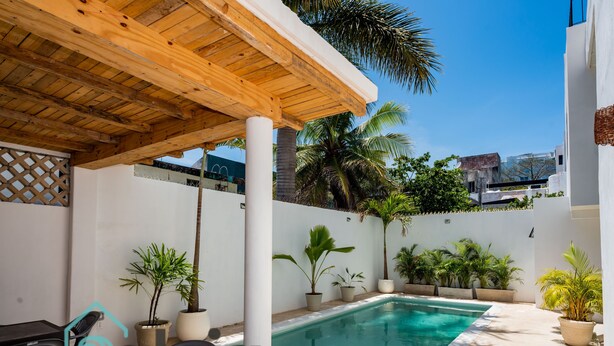 A pool area with a wooden pergola, potted plants, and a clear blue pool. - VICA GUEST HOUSE (Cancun)