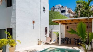 A white building with a pool, outdoor seating, and potted plants.