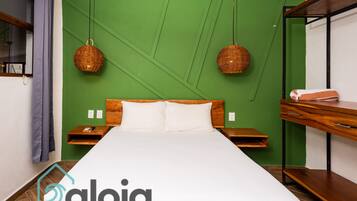 A neatly made bed in a room with green walls, two wicker wall hangings, a wooden nightstand, and a built-in bench with a towel.