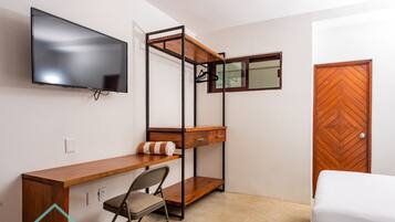 A compact room with a wooden desk, a chair, a bed, a TV mounted on the wall, and a wardrobe.