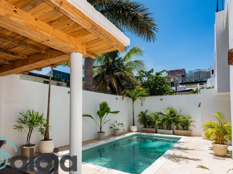 A pool area with a wooden pergola, potted plants, and a clear blue pool.