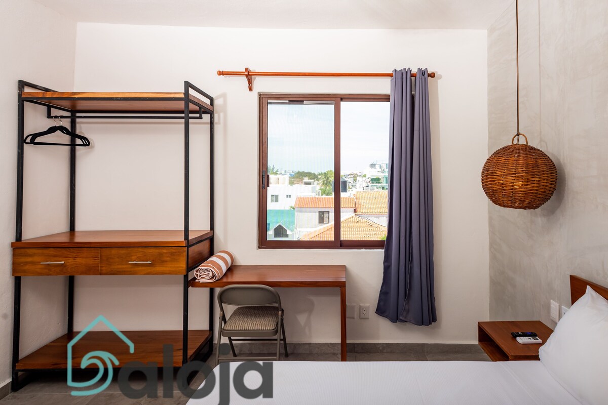 A bedroom with a bunk bed, a desk, a chair, a window with curtains, a hanging basket, and a bed with pillows.