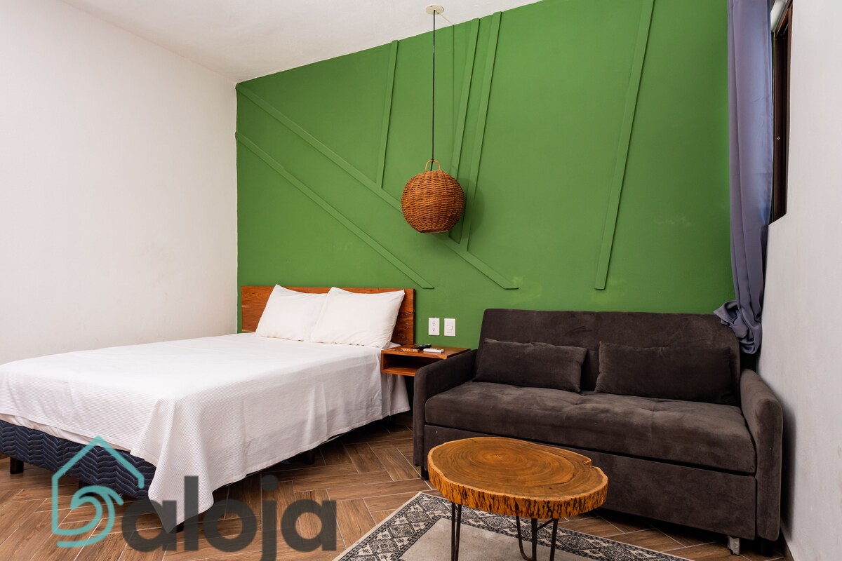 A modern room with a bed, a sofa, a round wooden coffee table, and a hanging basket.