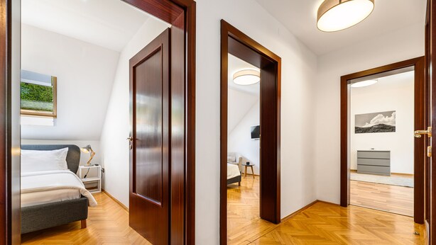 Habitación de hotel con cama, mesita de noche y vista a otra habitación por una puerta abierta.
