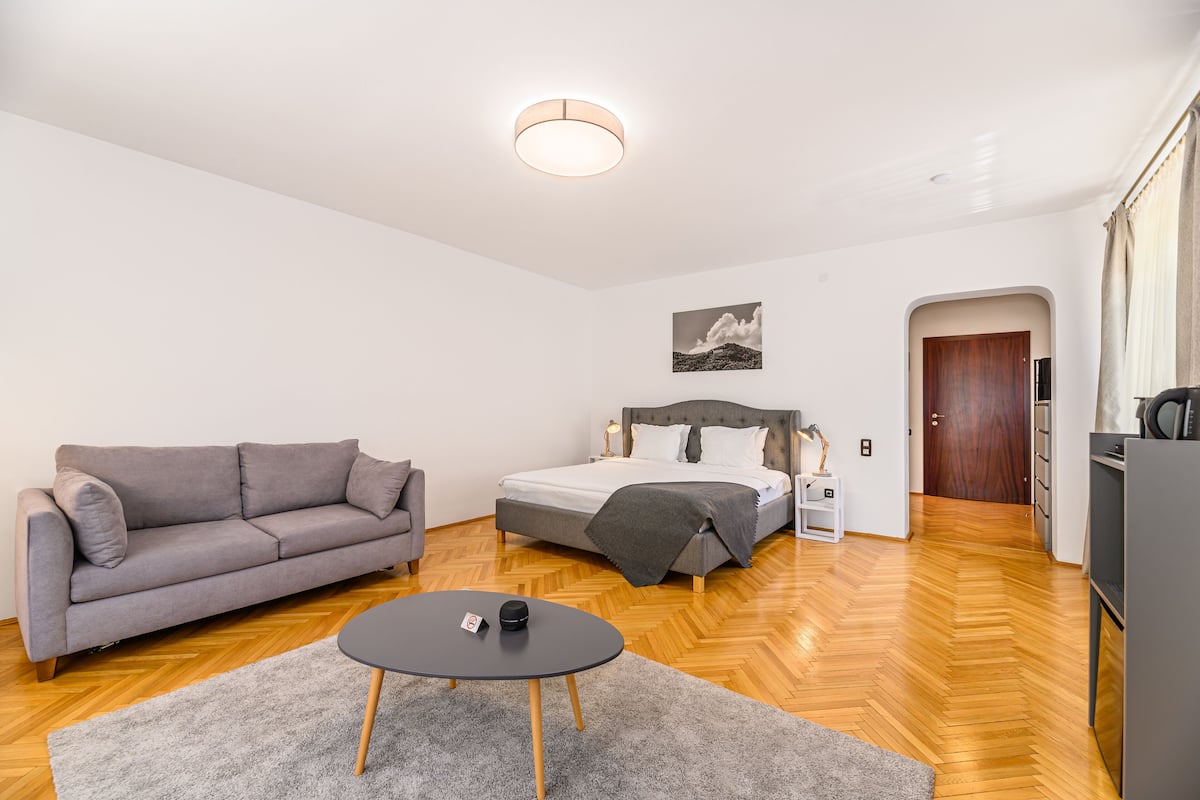 Un dormitorio moderno con una cama, un sofá gris, una mesita y suelo de madera.