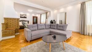 Una sala de estar moderna con un sofá seccional, una mesa redonda de centro, una chimenea y una zona de cocina al fondo.