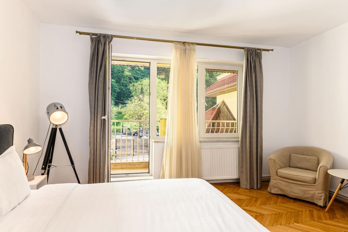 Una habitación de hotel con cama, una silla, una lámpara y un ventanal con cortinas.