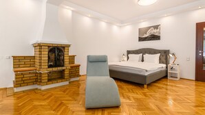 Un dormitorio con cama, una silla azul, chimenea y suelo de madera.