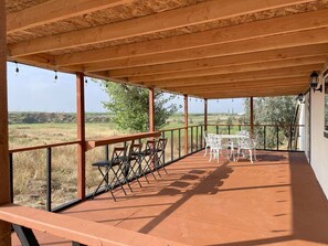 A covered outdoor patio with a table and chairs, overlooking a rural landscape.