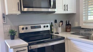 A kitchen with white cabinets, a stainless steel microwave, a stove, and a sink. - Modern wine country barn house (Temecula)