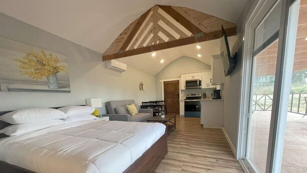 A bedroom with a large bed, a sofa, and a dining area with a kitchen in the background. - Modern wine country barn house (Temecula)