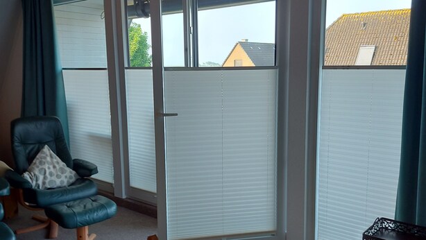 Ein Zimmer mit Holzboden, einem Holzesstisch, einem blauen Stuhl mit Kissen, einem weiteren Holzstuhl und Blick durch eine Schiebetür nach draußen.
