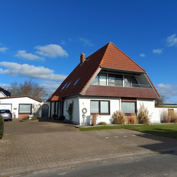 A two-story house with a red-tiled roof, a garage, and a paved driveway.