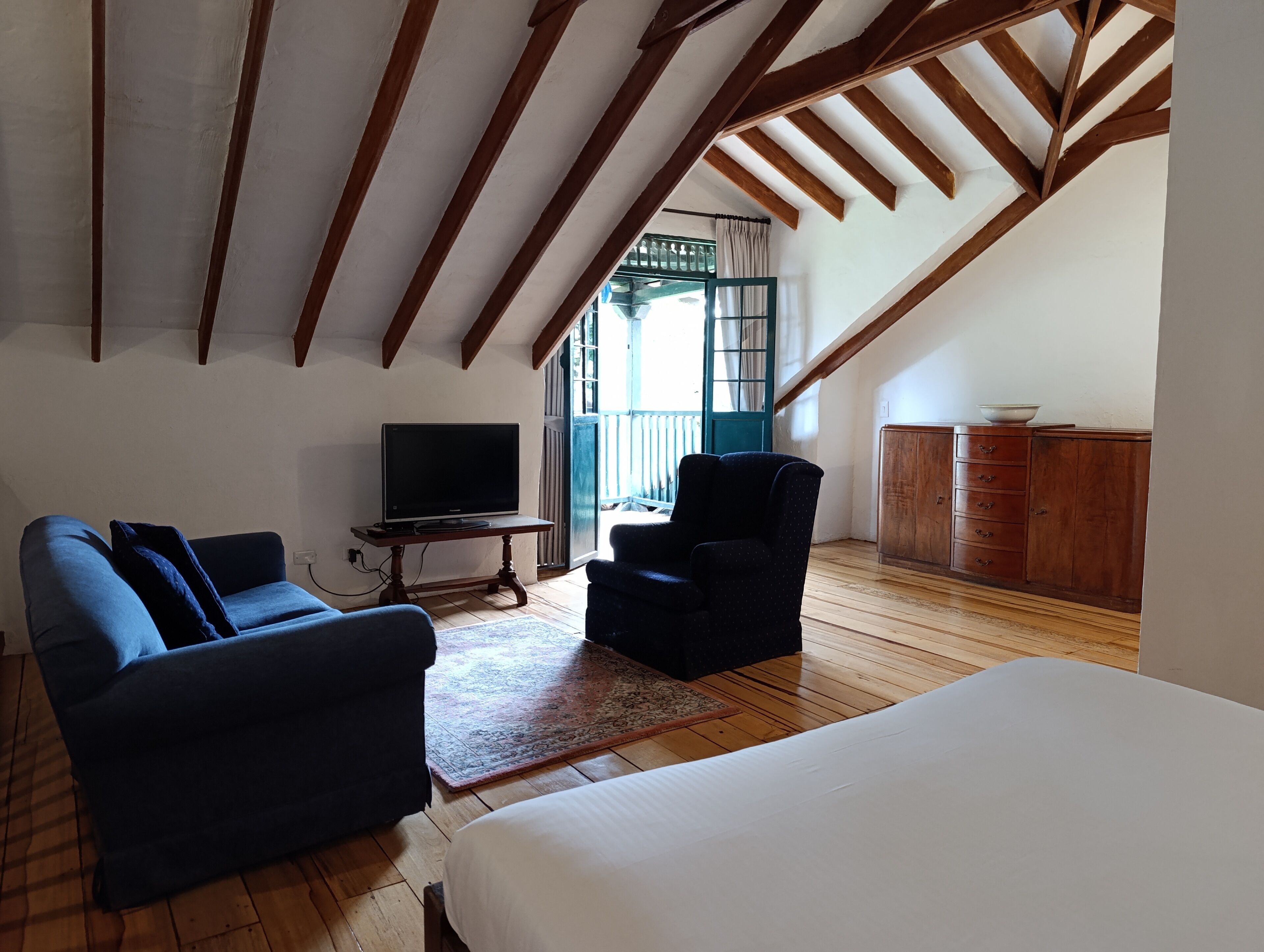 A room with a wooden ceiling, a television on a wooden table, a sofa, a chair, and a cabinet.