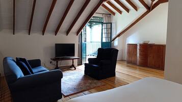 A room with a wooden ceiling, a television on a wooden table, a sofa, a chair, and a cabinet.