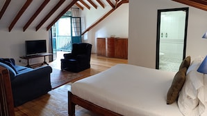 A bedroom with a wooden ceiling, a bed, a TV, a chair, and a view of a bathroom through an open door. - Hotel Hacienda el Novillero (Fusagasugá)