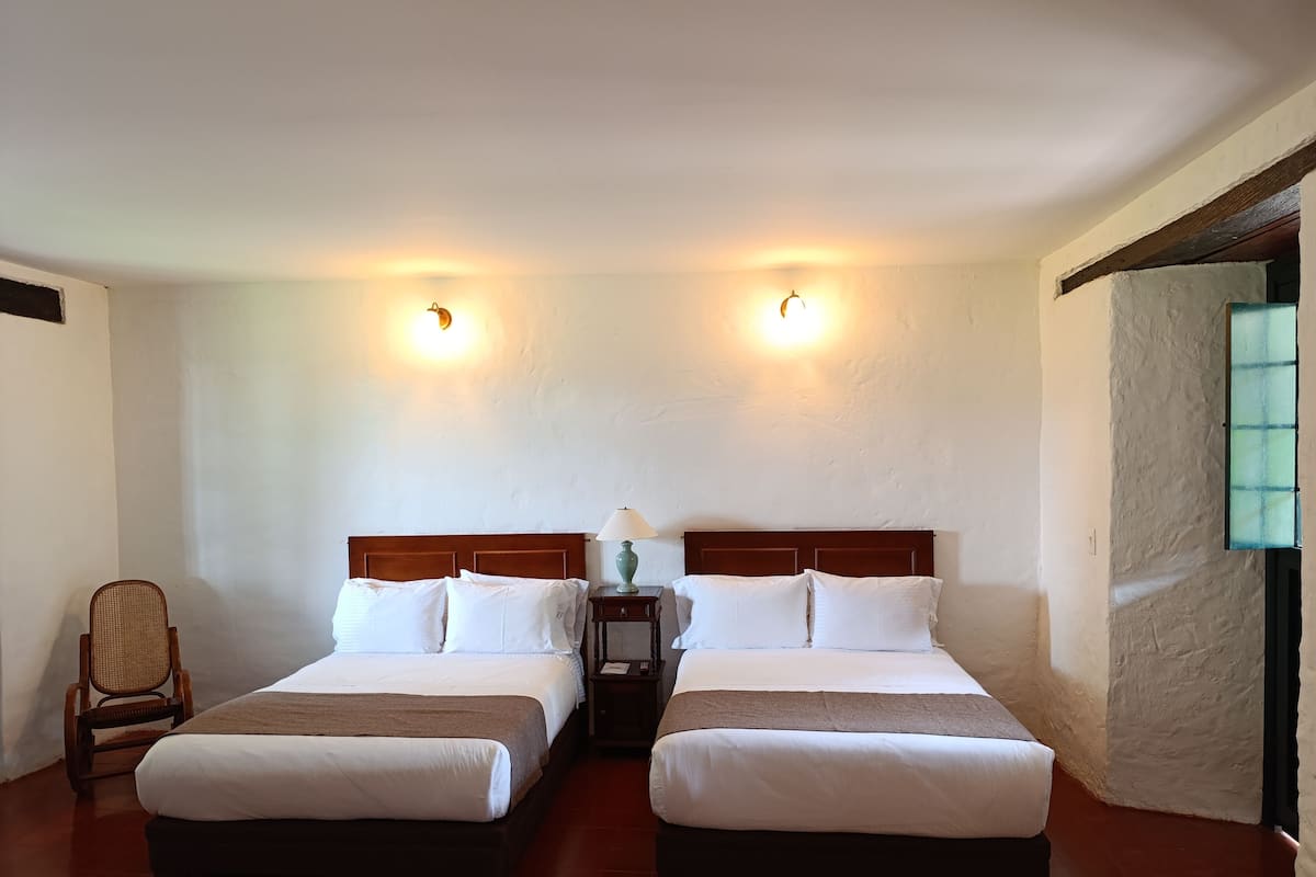 Une chambre avec deux lits, une chaise, une table de chevet et une lampe fixée au mur.