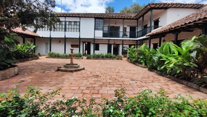 A courtyard with a fountain, surrounded by potted plants and a building with a tiled roof and balconies. - Hotel Hacienda el Novillero (Fusagasugá)