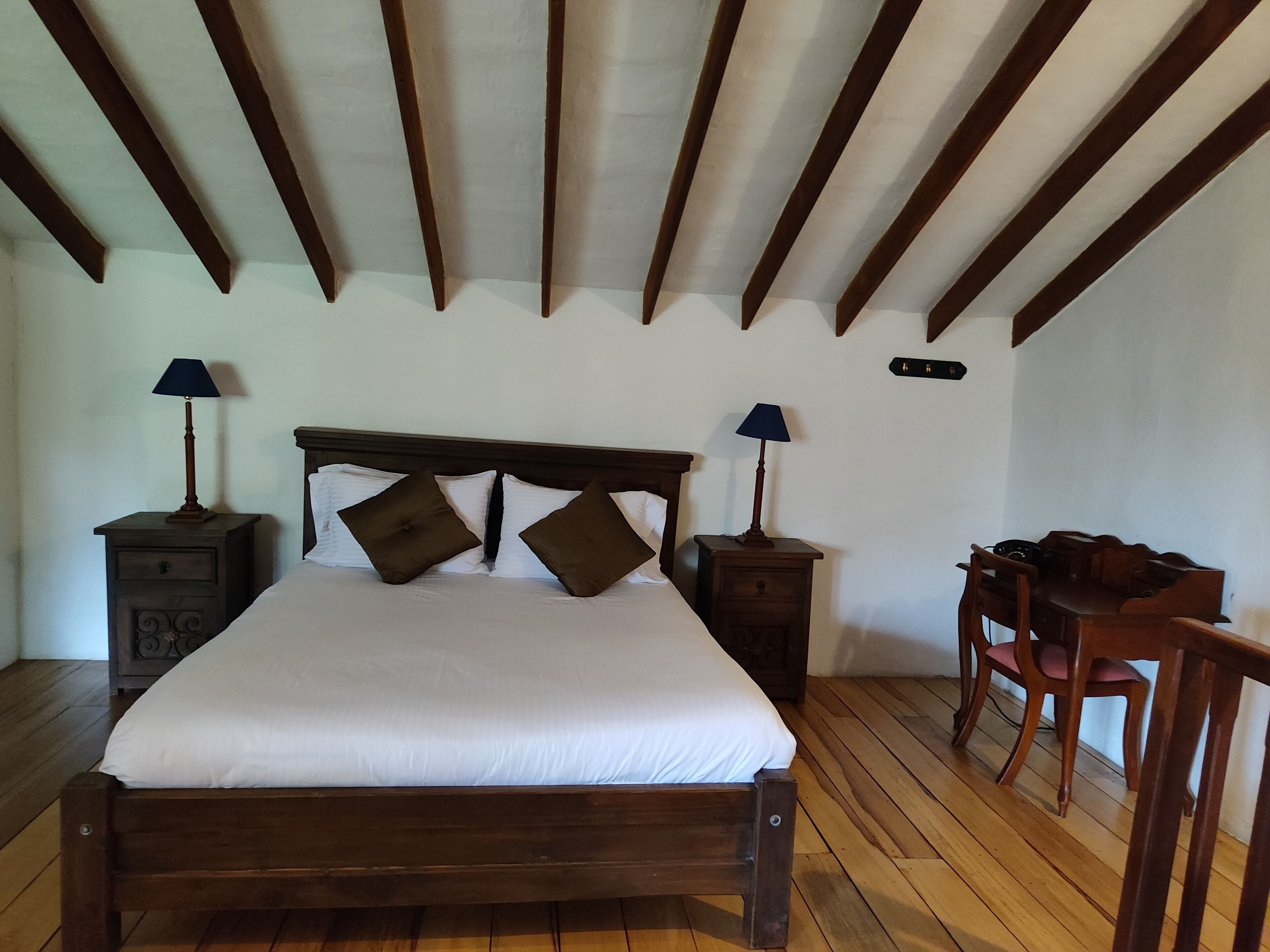 Un dormitorio con una cama de madera, dos mesitas de noche con lámparas, una silla de madera y un escritorio de madera.