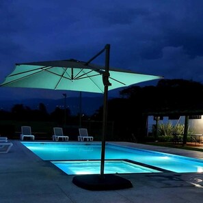 Une piscine dotée d’un grand parasol et de chaises longues.