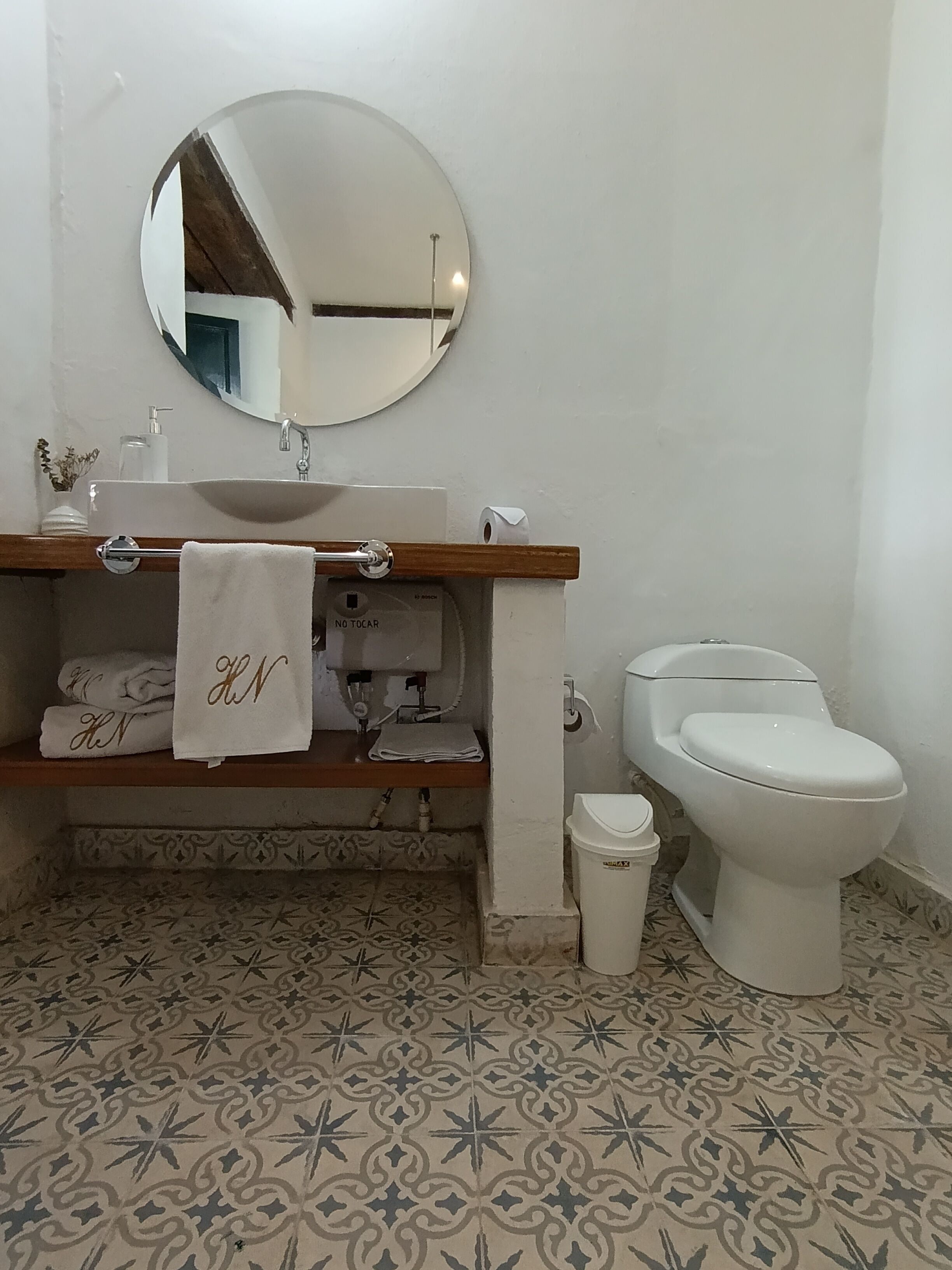 Een badkamer met een wit wastafel, spiegel en toilet. Er liggen handdoeken met initialen op de handdoekhouder.