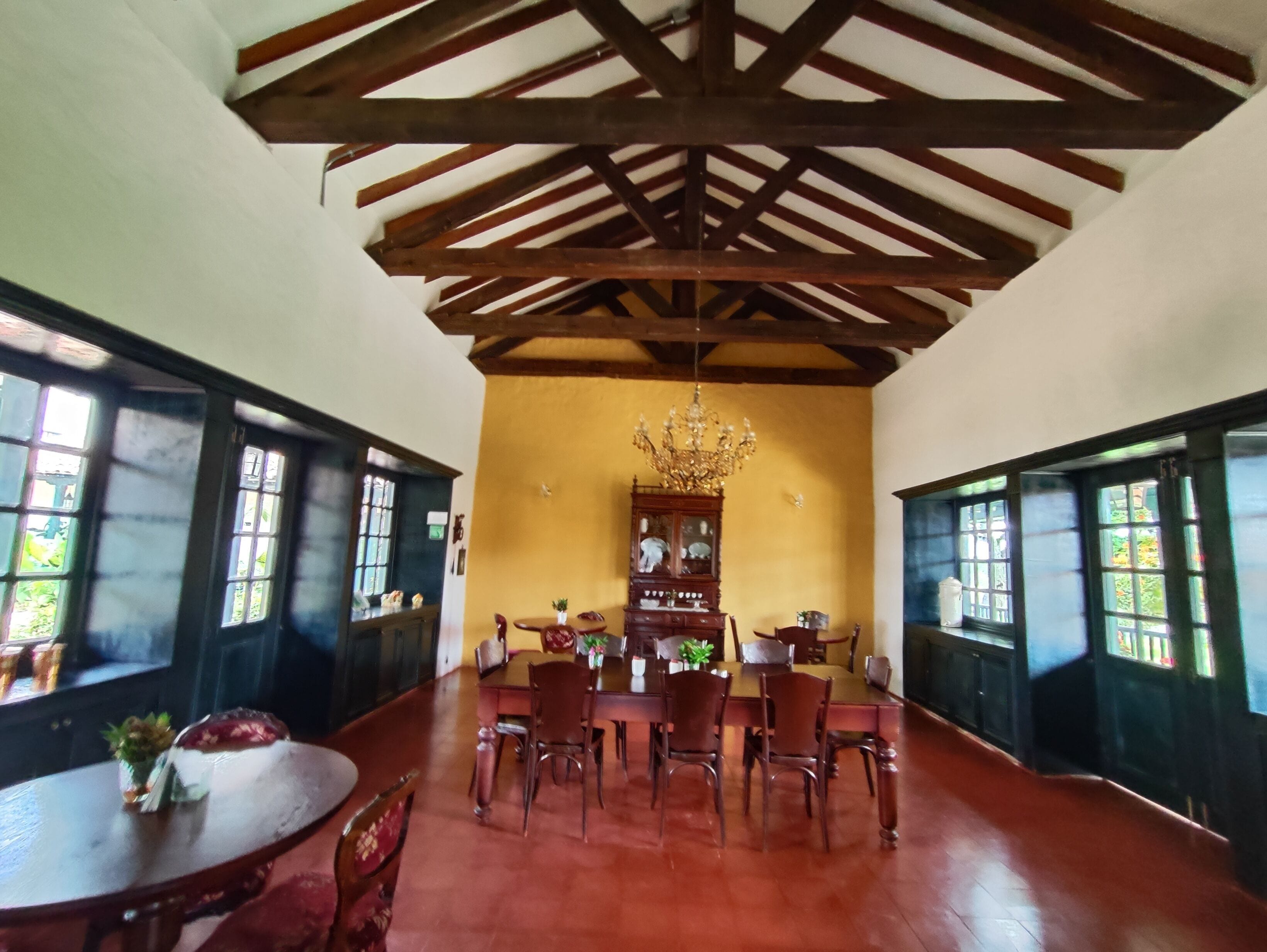 Zona pranzo con soffitto alto, travi in legno, un lampadario e un ampio armadio in legno.