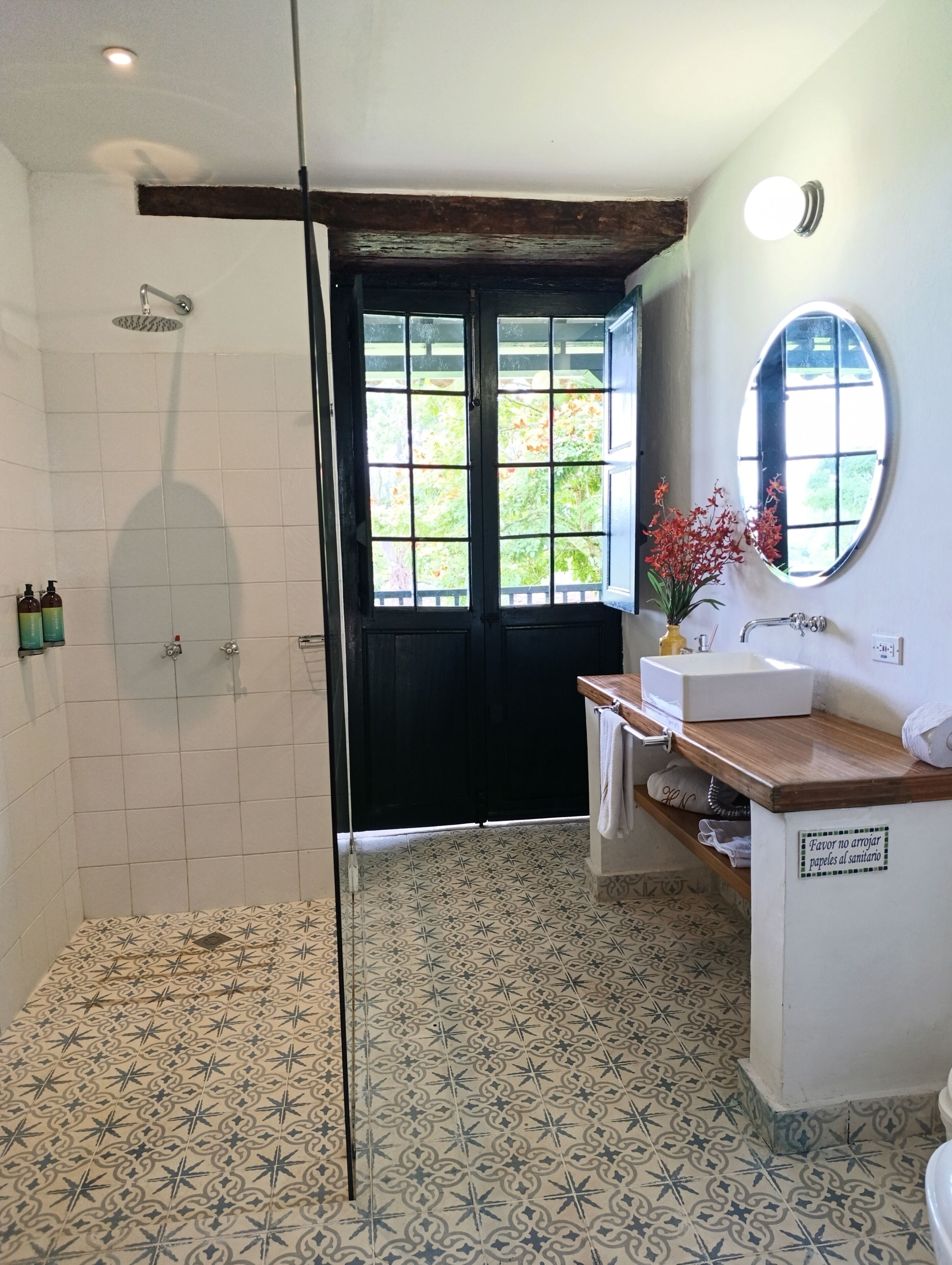 Een badkamer met een douche, wastafel, spiegel en vloertegels met een patroon.