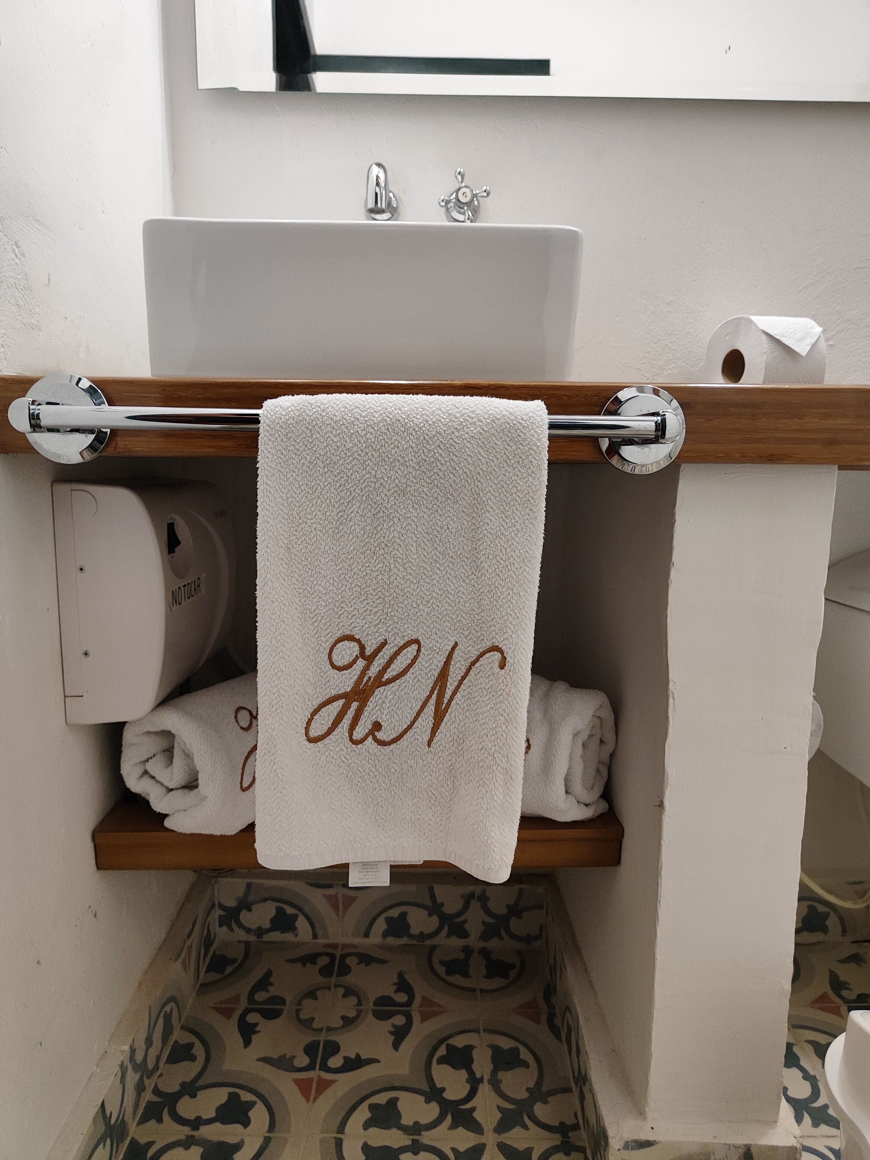 Ein Badezimmer mit einem weißen Waschbecken, einem Handtuchhalter mit einem weißen Handtuch und einem Toilettenpapierhalter.