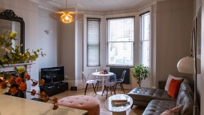 A modern living room with a sofa, ottoman, and a dining table with chairs. - Gorgeous 2-bed Apartment With Patio (Brighton)
