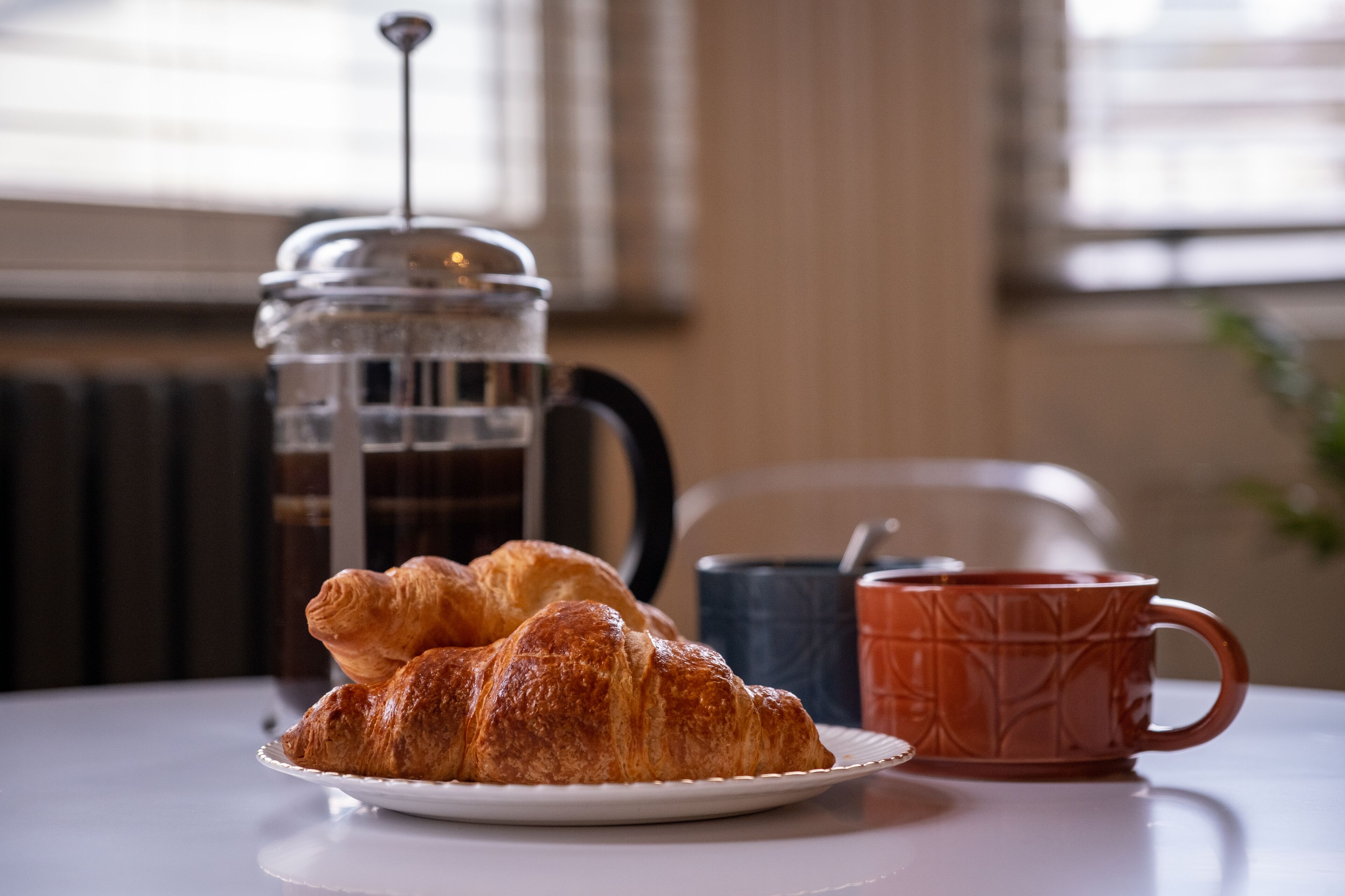 Ein Teller mit Croissants, eine Kaffeekanne und eine Tasse auf einem Tisch.