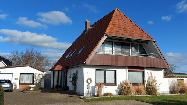 A two-story house with a red-tiled roof, a garage, and a paved driveway. - 2-zimmerwohnung in Direkter Strandnähe (Westerdeichstrich)