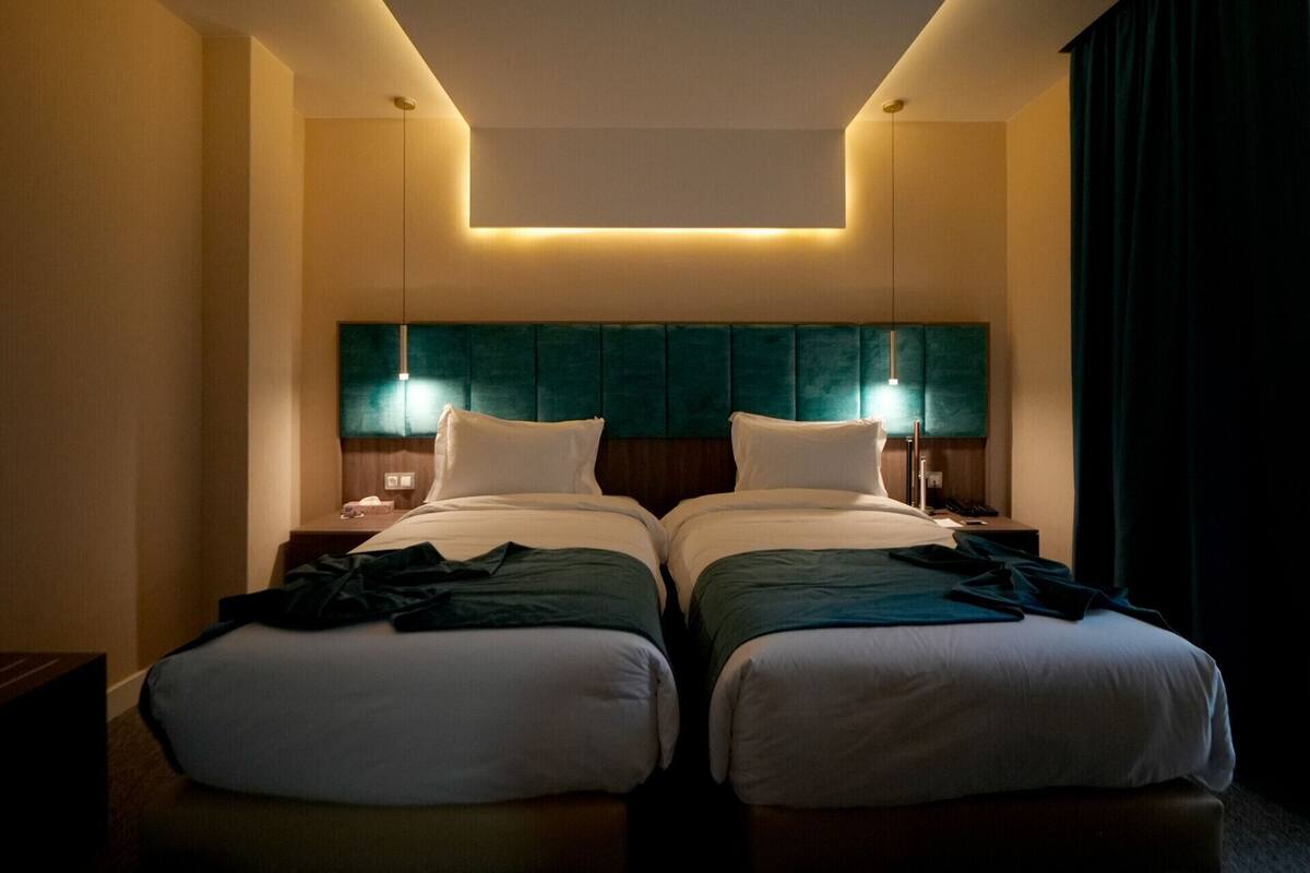 A hotel room with two beds, a teal headboard, bedside lamps, and a modern ceiling design.