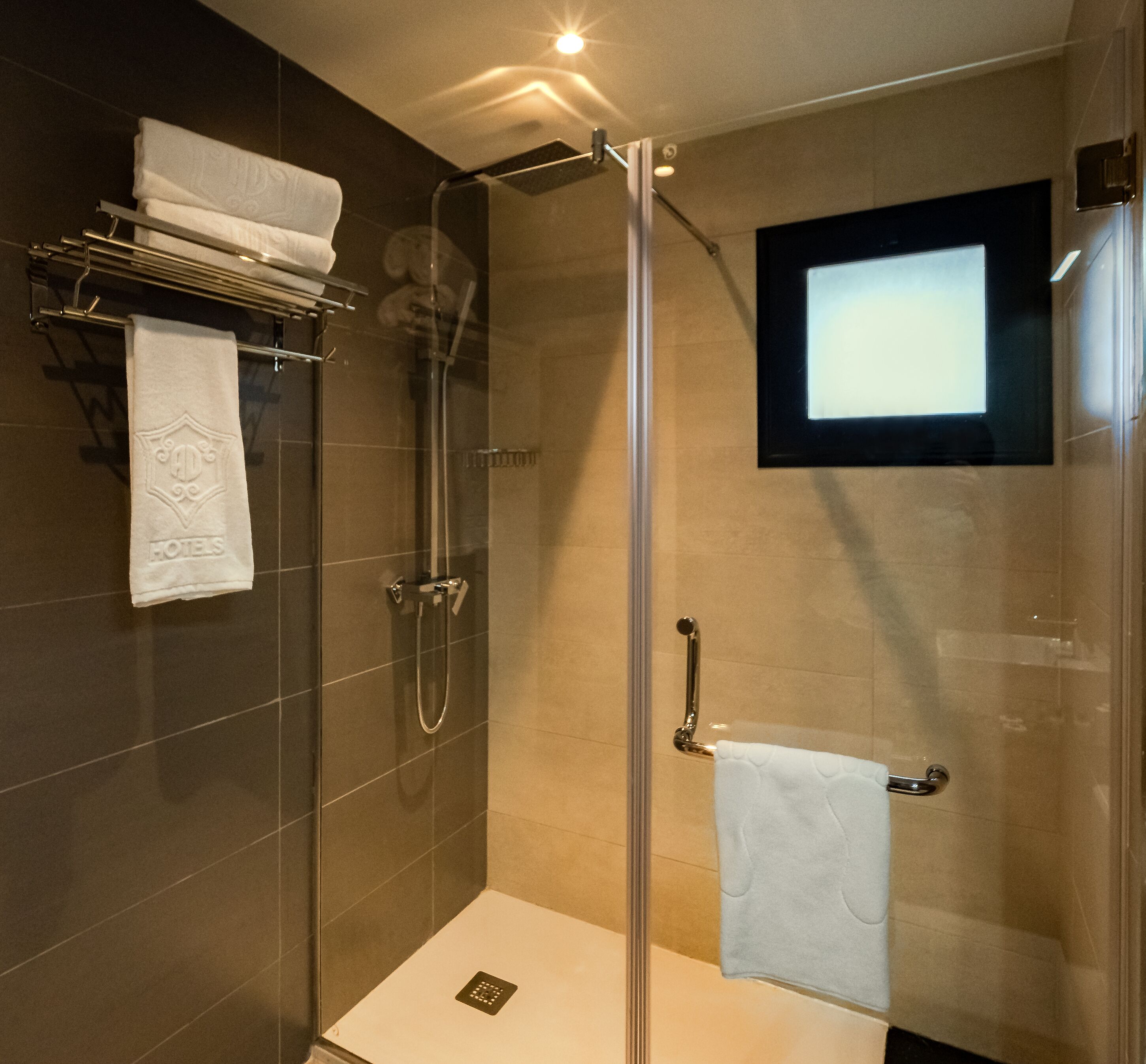 A modern shower area with a glass door, a handheld showerhead, a wall-mounted towel rack, and a built-in TV screen.