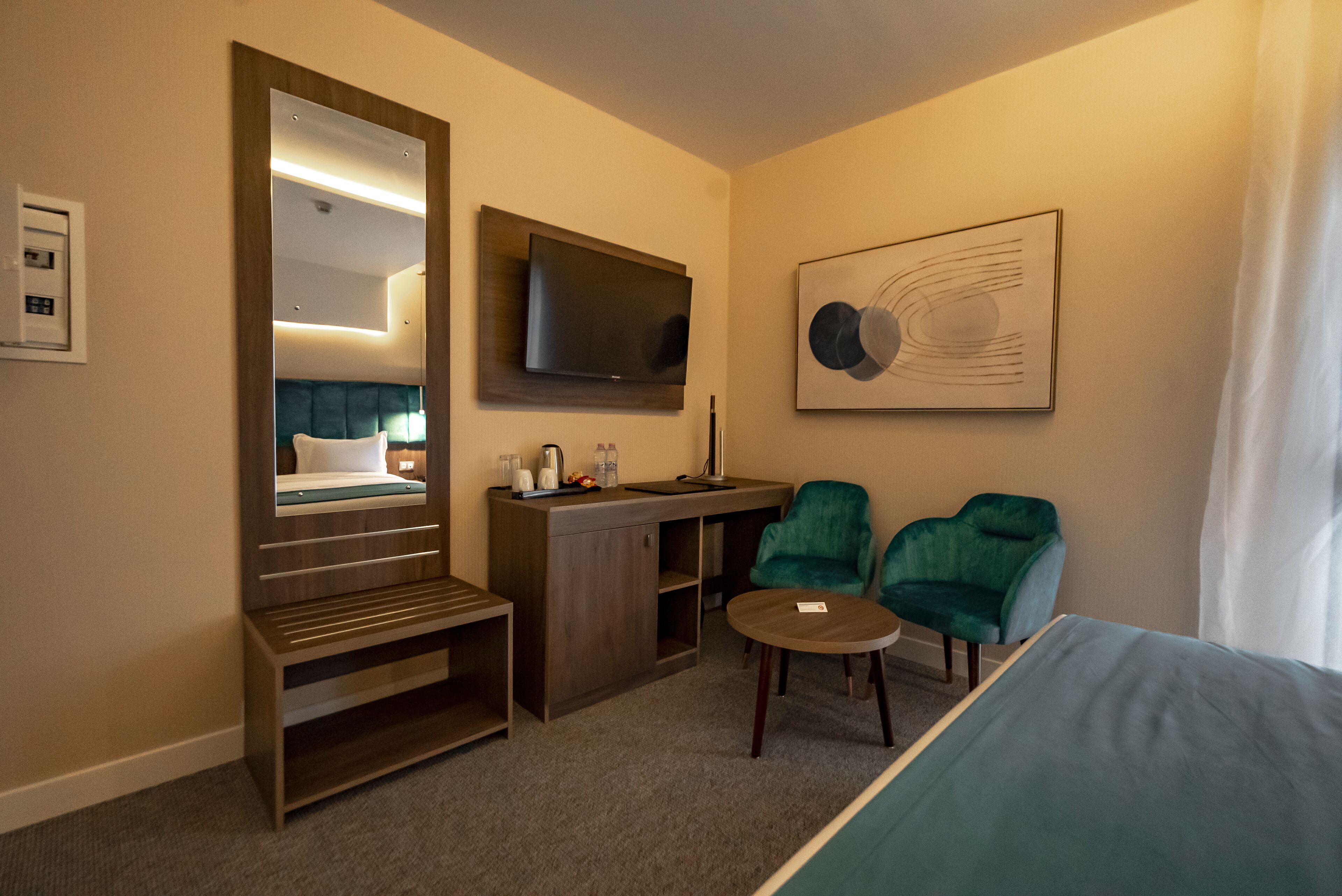 Hotelkamer met een bed, een bureau, een stoel, een klein tafeltje, een televisie en een grote spiegel.