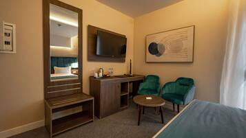 Hotelkamer met een bed, een bureau, een stoel, een klein tafeltje, een televisie en een grote spiegel.