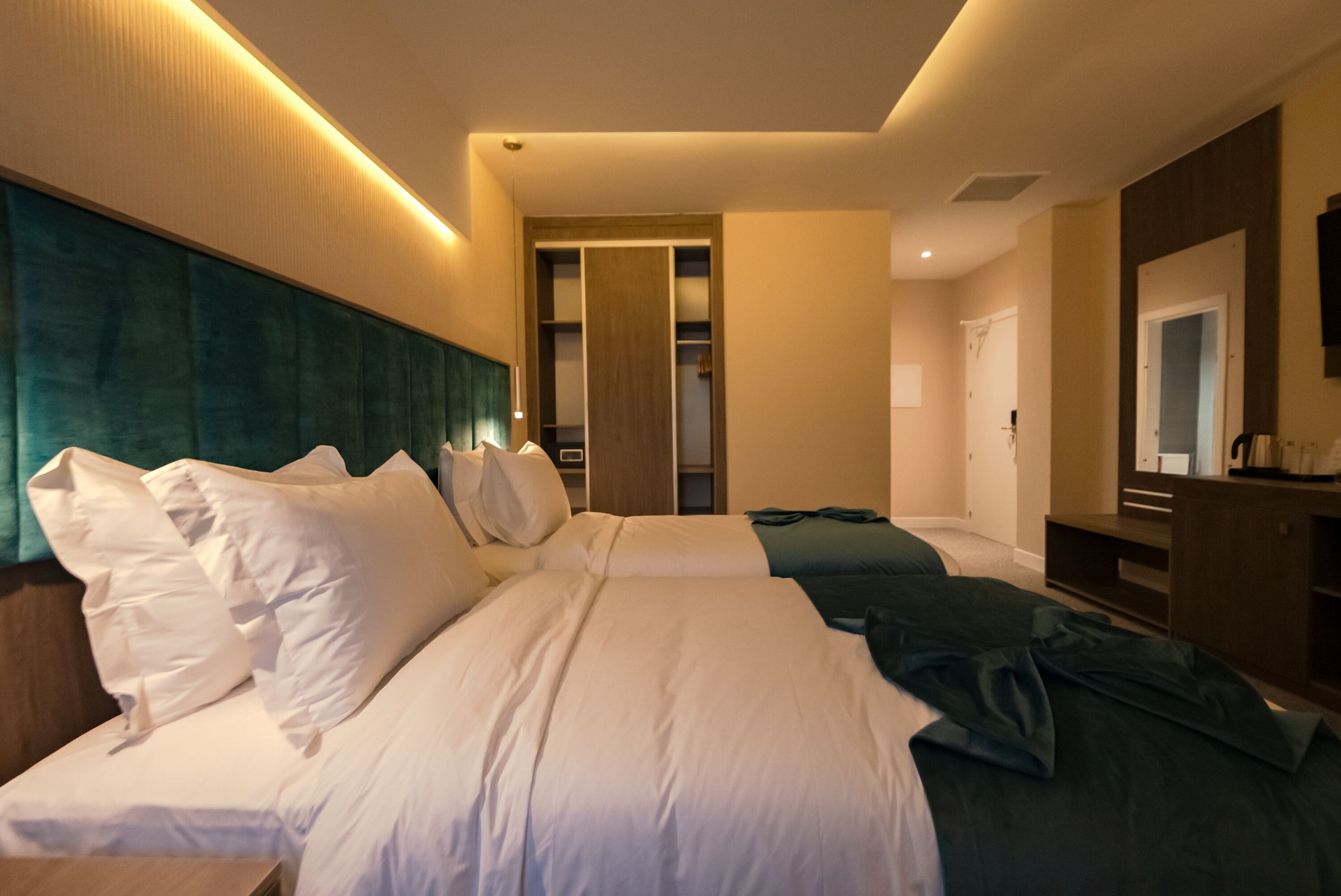 A hotel room with two beds, a wardrobe, a mirror, and a television.