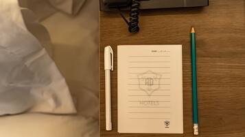 Een hotelkamer met een houten bureau, een telefoon, een notitieboekje met hotel logo, een pen en een potlood.